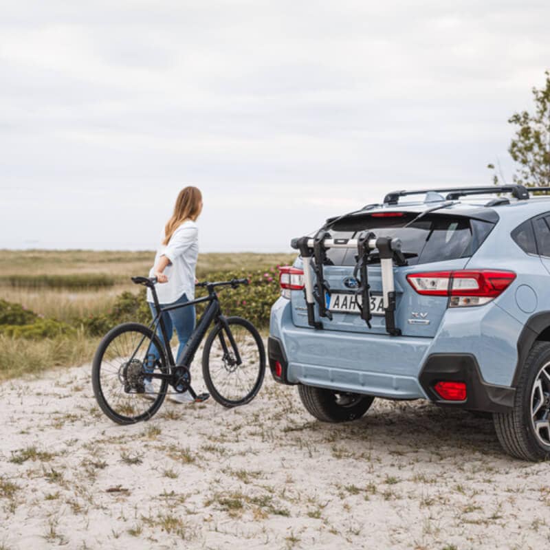 Woman holding bike next to car with rear mounted Thule bike racks